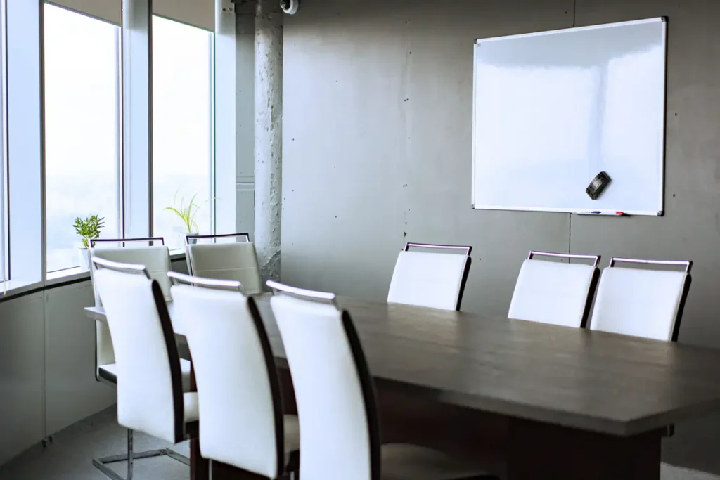 Empty, sunlit office conference room with chairs, meeting table, and whiteboard