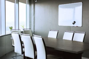 Empty, sunlit office conference room with chairs, meeting table, and whiteboard